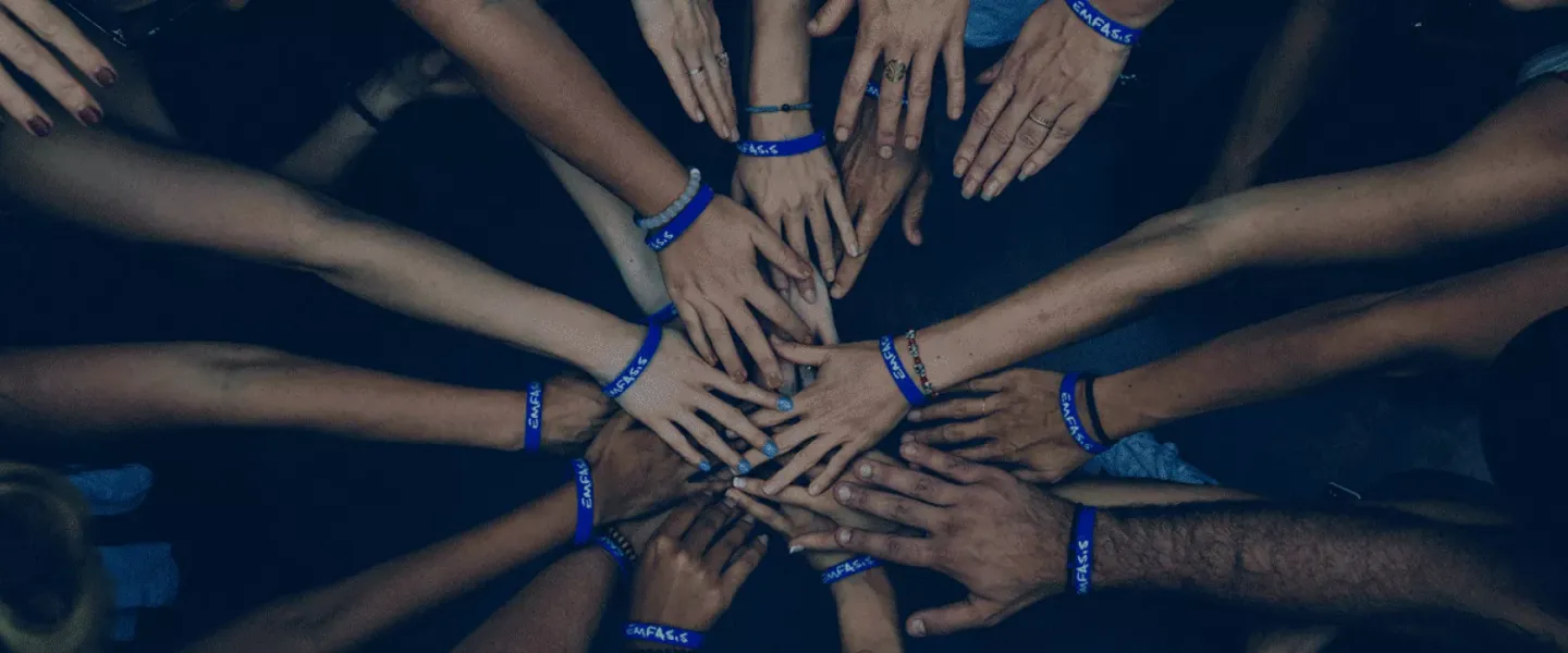 Hands of all genders and ages held into a circle, with all hands touching in the middle.