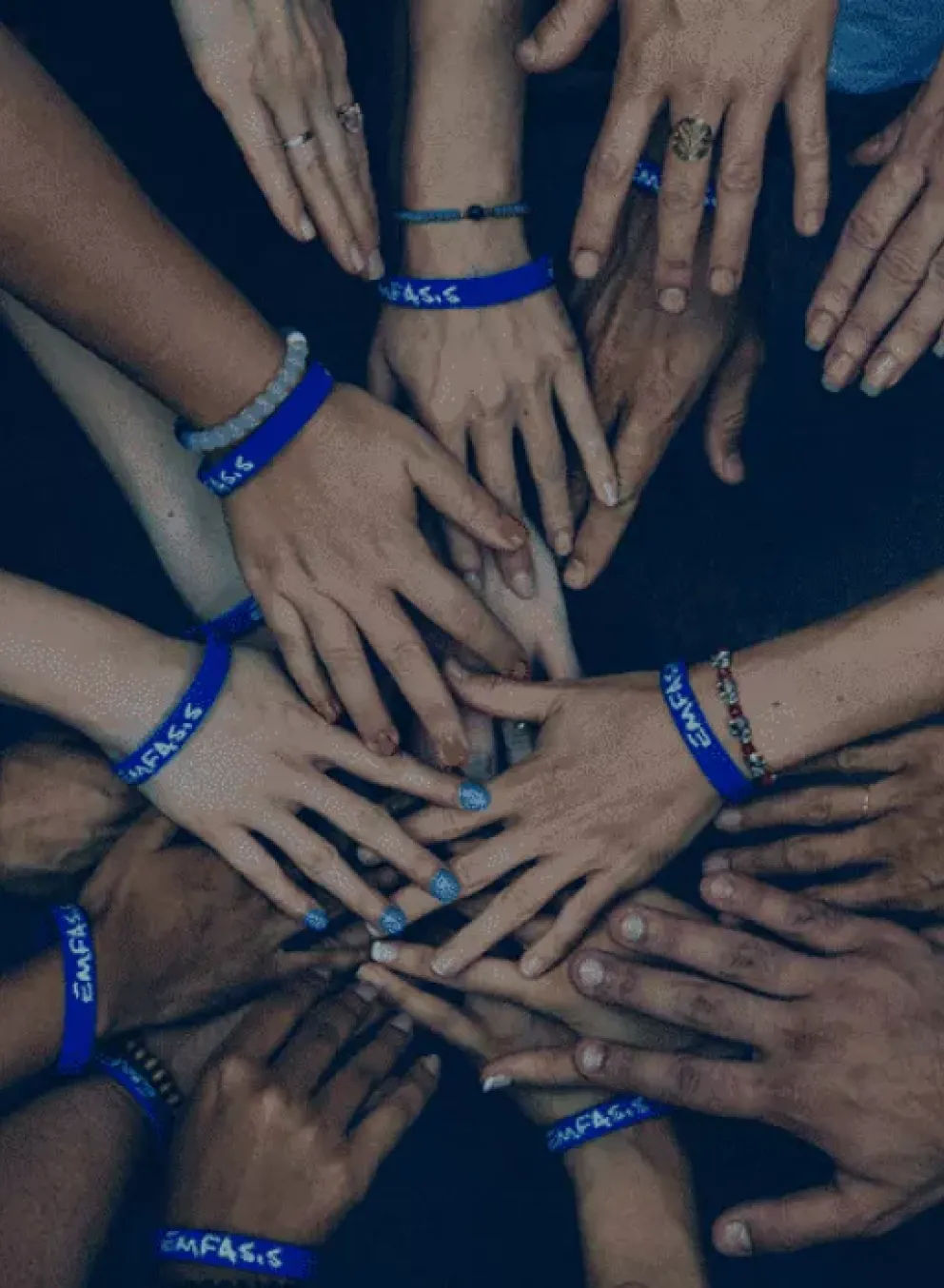 Hands of all genders and ages held into a circle, with all hands touching in the middle.