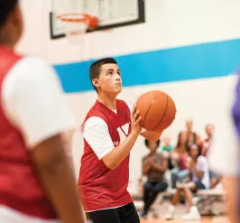 Boy shooting basketball with crowd in the background