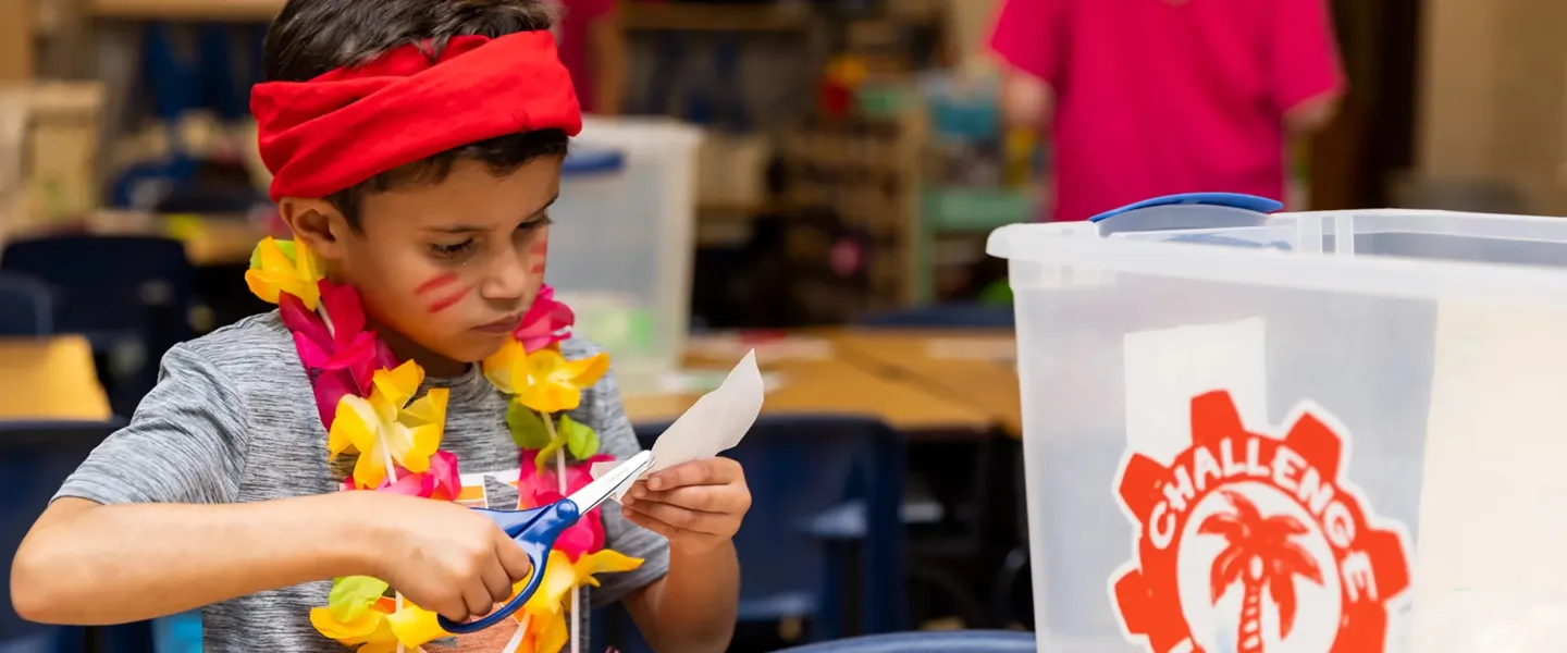 Child using scissors to craft during a challenge island class