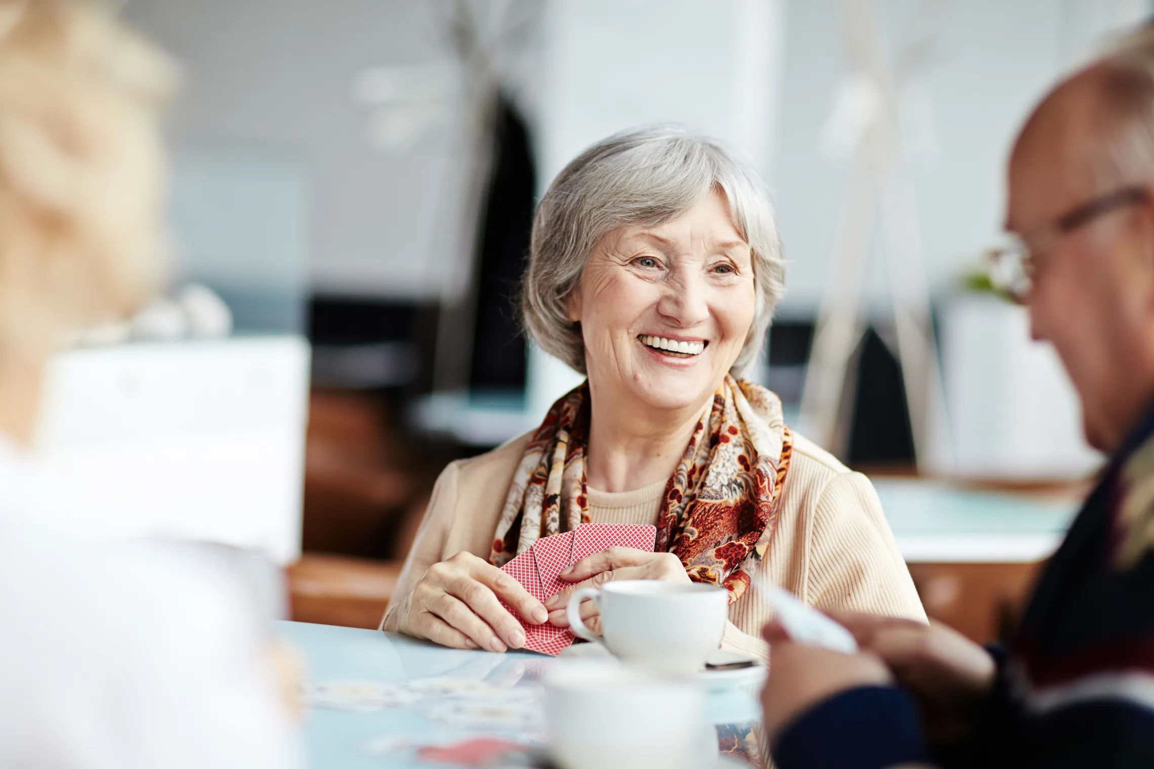 Smiling senior woman playing cards and enjoying coffee with friends
