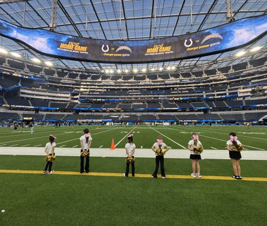6 cheerleader standing at the edge of the football field