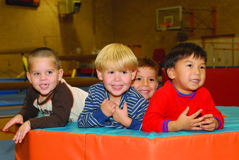 A group of young boys lay down smiling at a camera on a gymnastics mat.