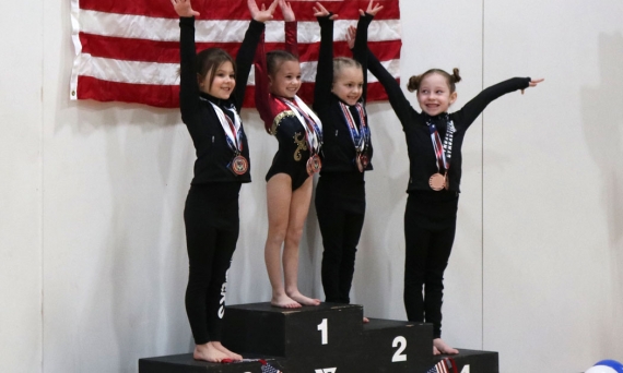 Gymnasts on platform with their medals in fron of American Flag