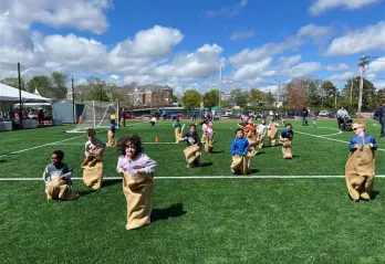 large group of children racing in potato sacs jumping toward the camera