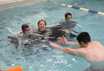 3 participants with swim instructor in the pool during class
