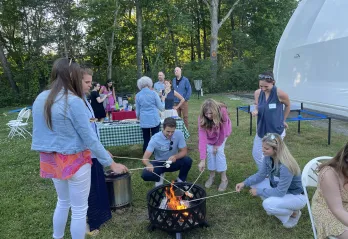 Party goers roast marshmallows over a fire at Camp Chickami