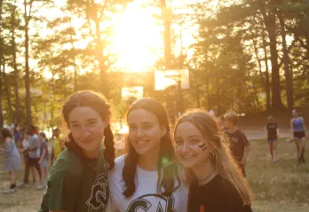 Three campers sand awaiting the closing ceremony as the sun begins to set. 