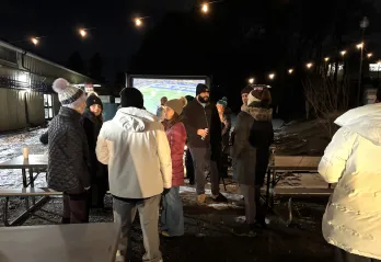 group of adults outside with string lights and large screen of football