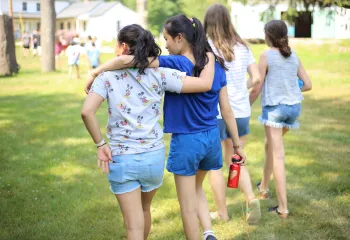Two girls walking across a grassy field with their arms draped over each other