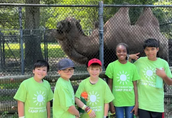 camp pikati campers pose in front of a camel at the zoo