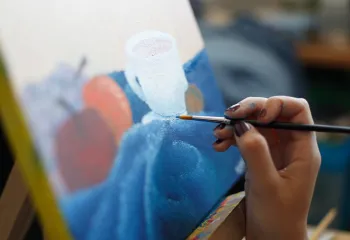 a hand holding a paintbrush in front of a painting
