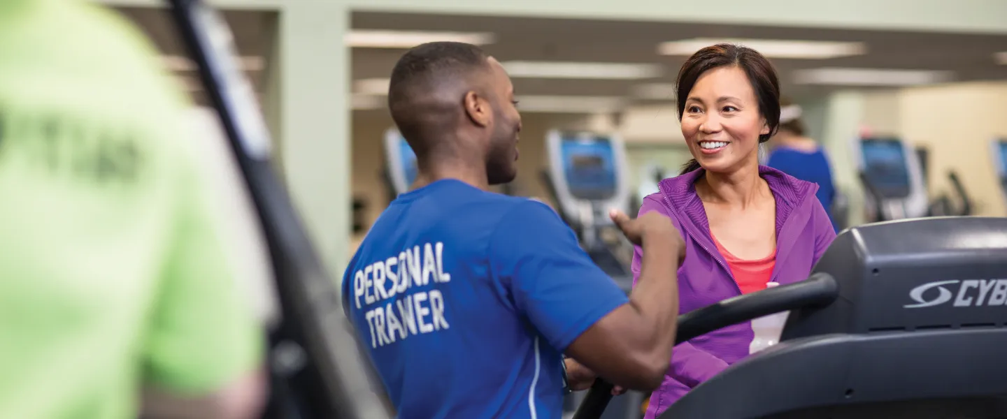 A personal trainer talks to a smiling woman who is on a treadmill