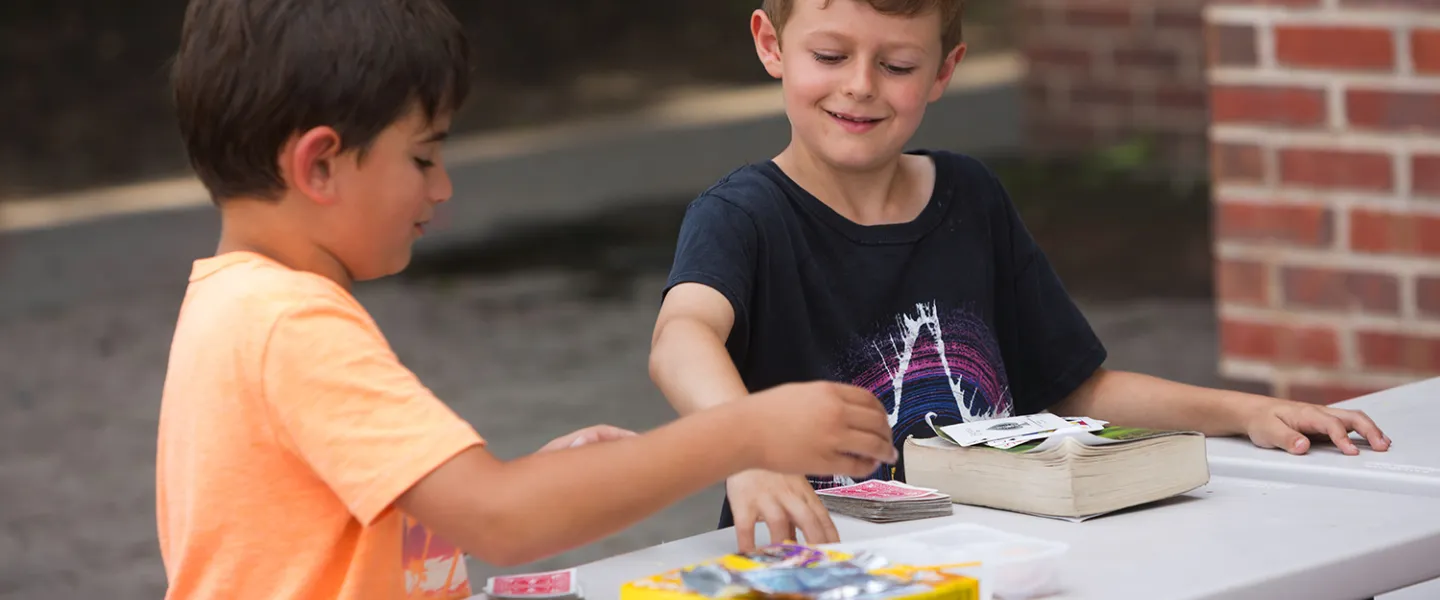 Two school-age boys smile while playing a card game