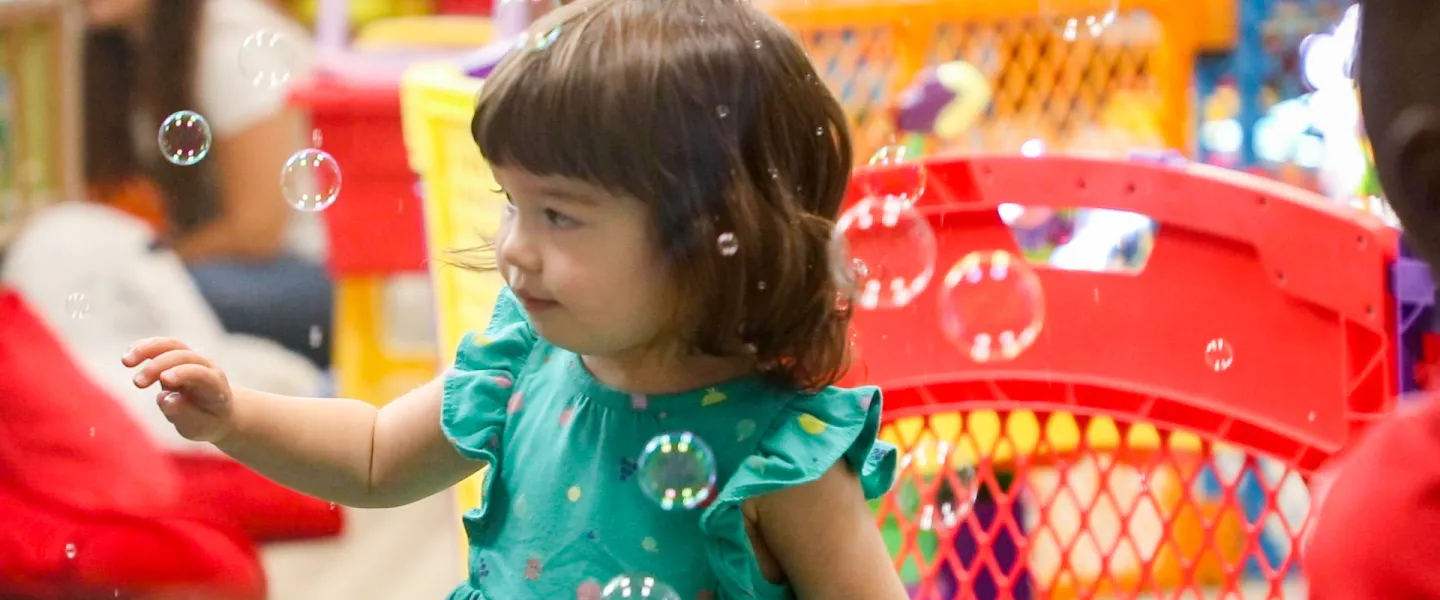 Young girl looks curiously at bubbles in a bright indoor play area.
