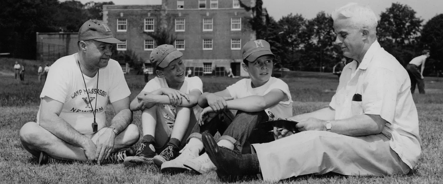 Two men and two boys sit on the grass outside the YMCA 