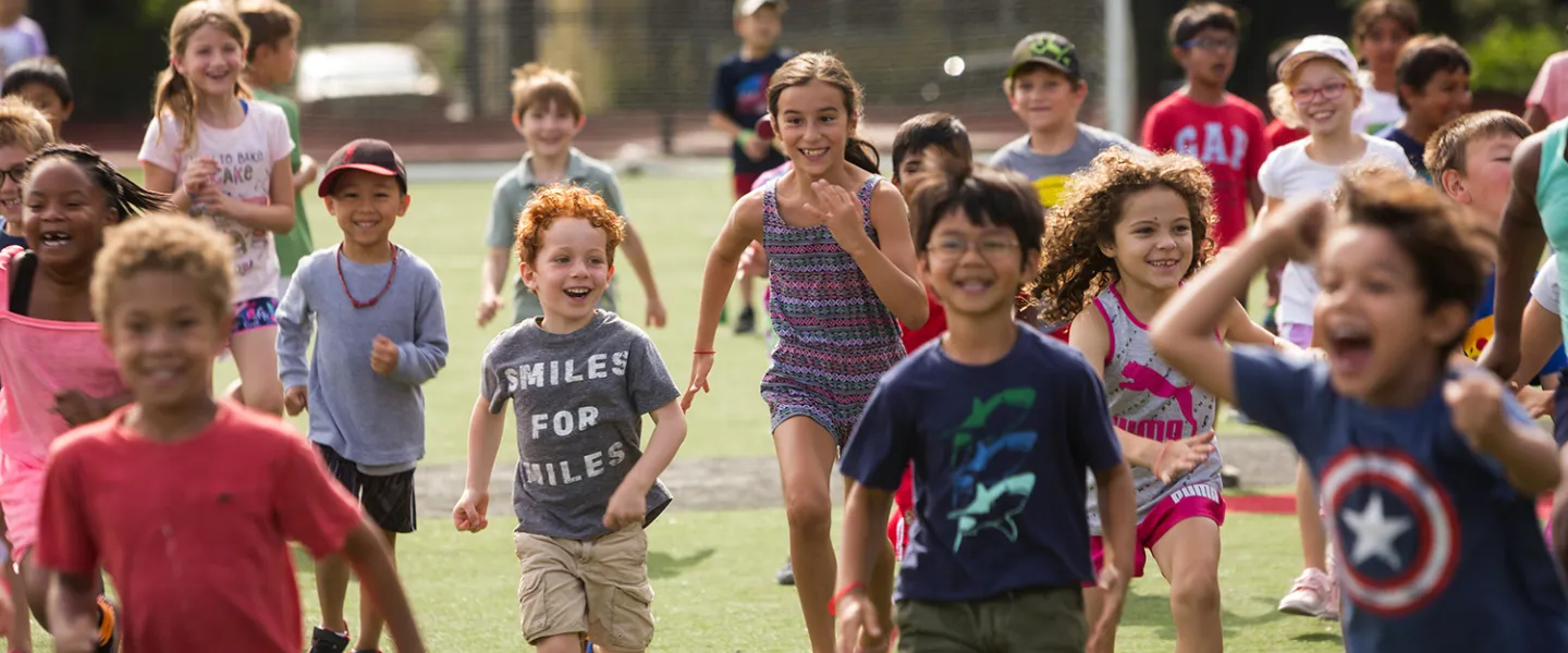A group of school-age kids run across a field laughing and smiling