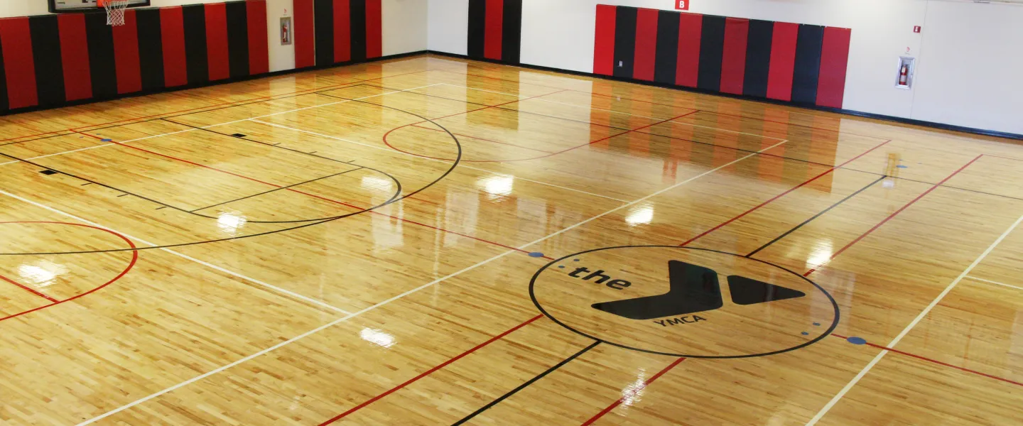 A large gymnasium with basketball hoops and a YMCA logo in center court