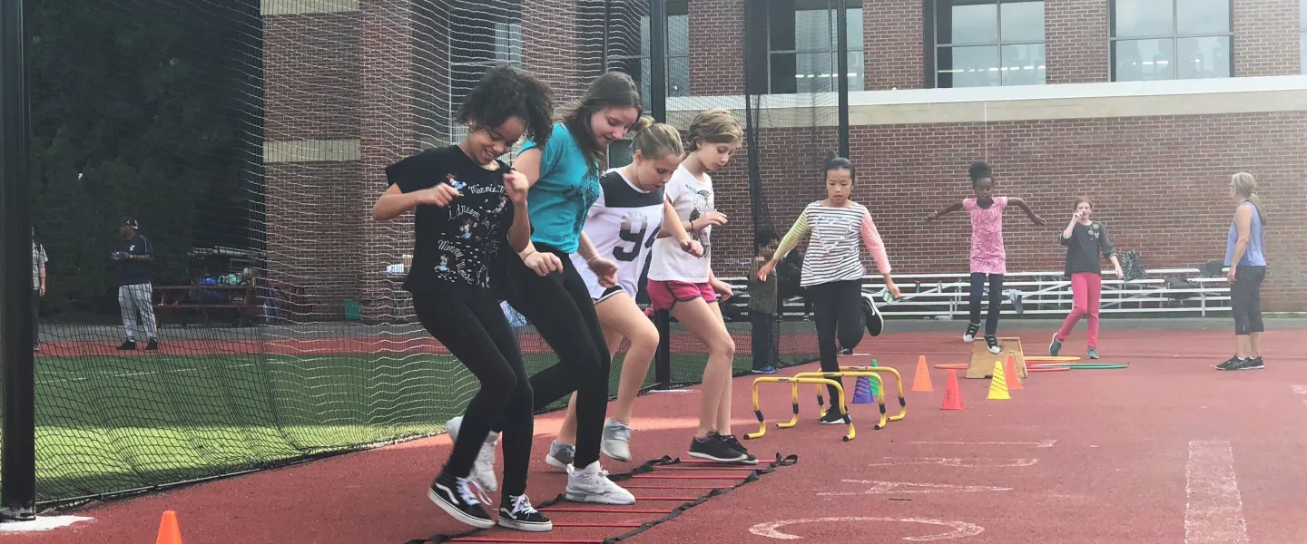 A group of preteen girls shuffle through a fitness obstacle course