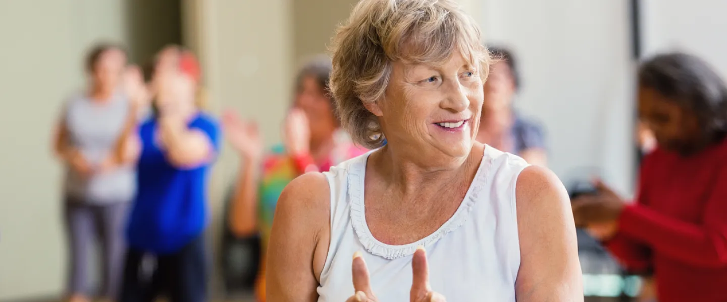 An older woman in focus claps along in a group exercise class