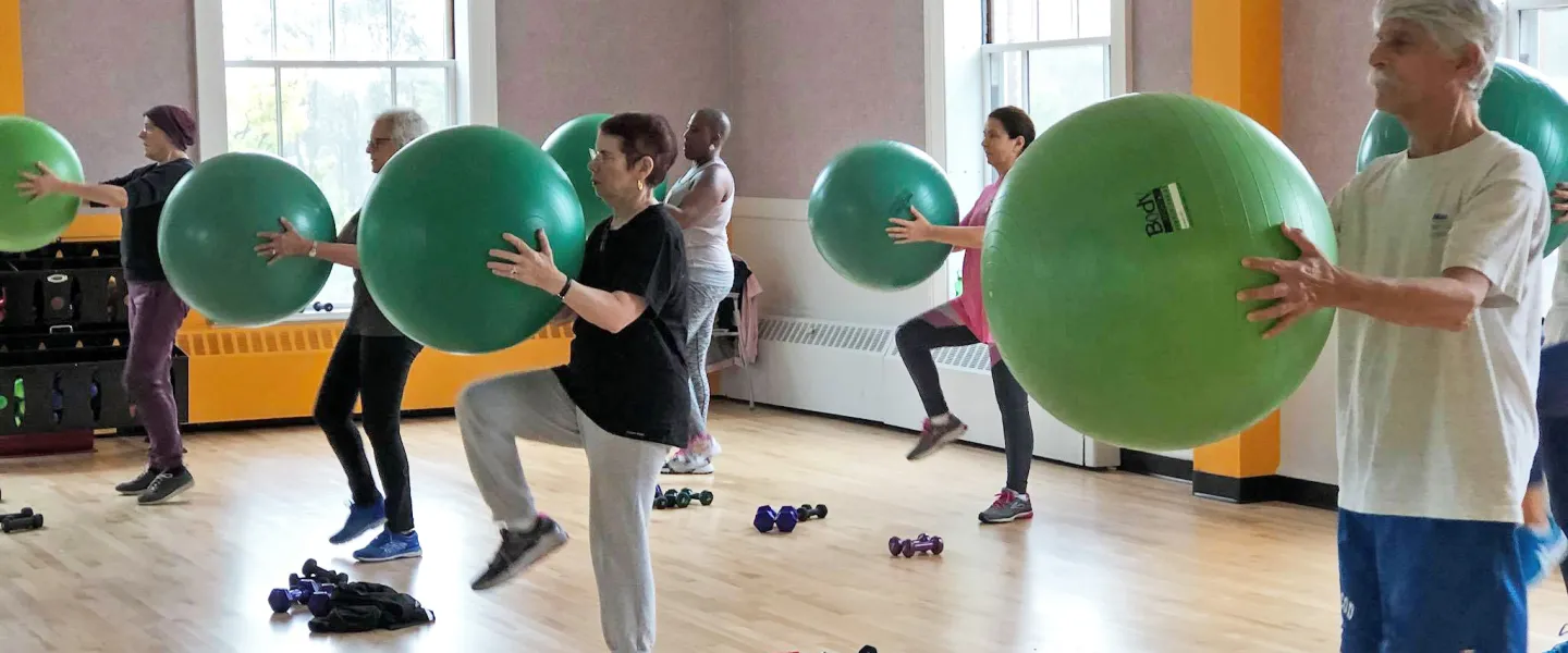 A group of older adults in an exercise class hold stability balls in front of them