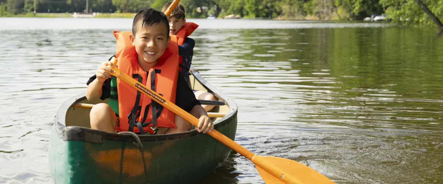 A camper smiles at the camera while paddling a canoe
