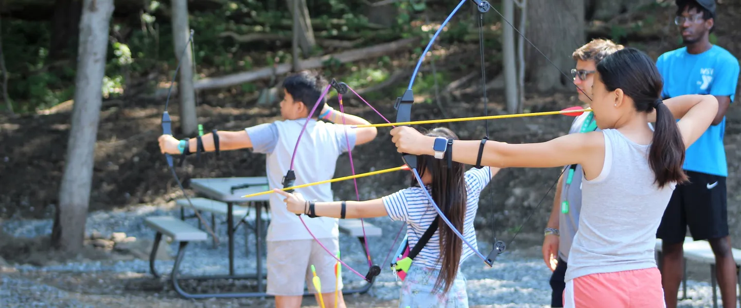 three campers at Camp Wells hold bows and arrows and prepare to shoot