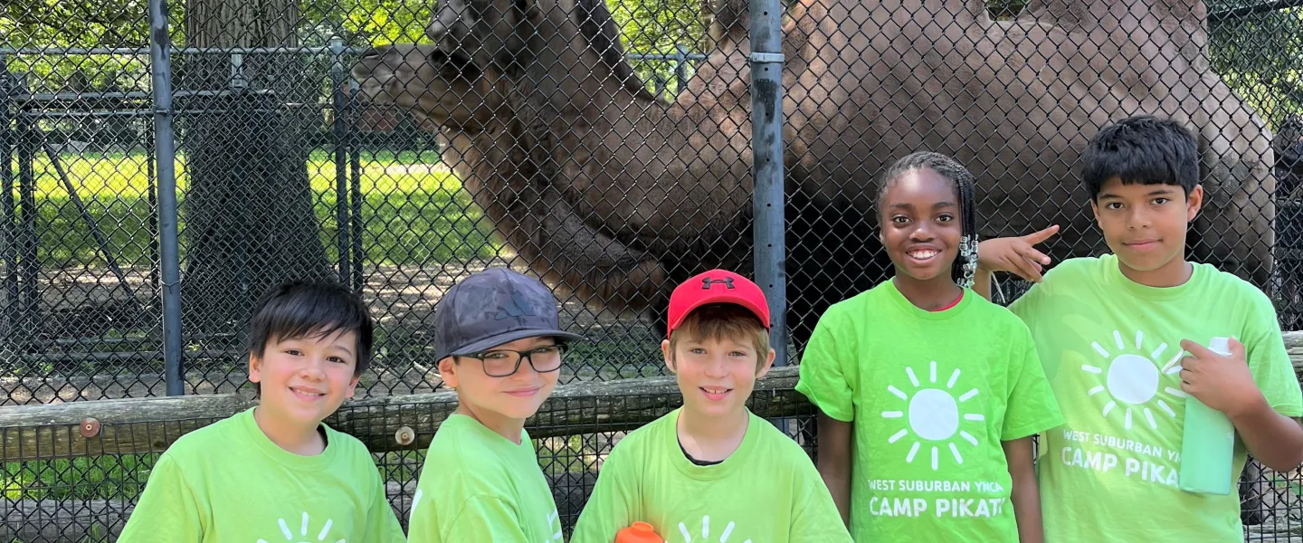 camp pikati campers pose in front of a camel at the zoo