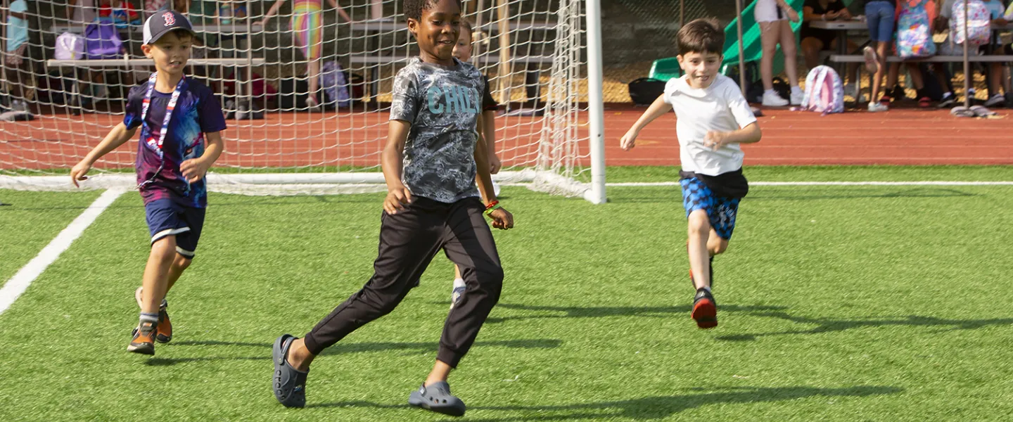 A couple campers running after the soccer ball during a game.