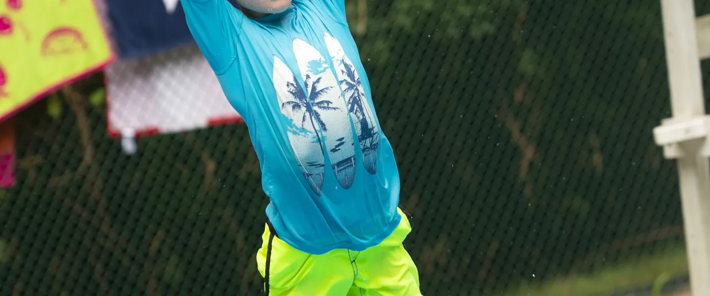 A camper jumping into the pool with his arms stretched all the way up.