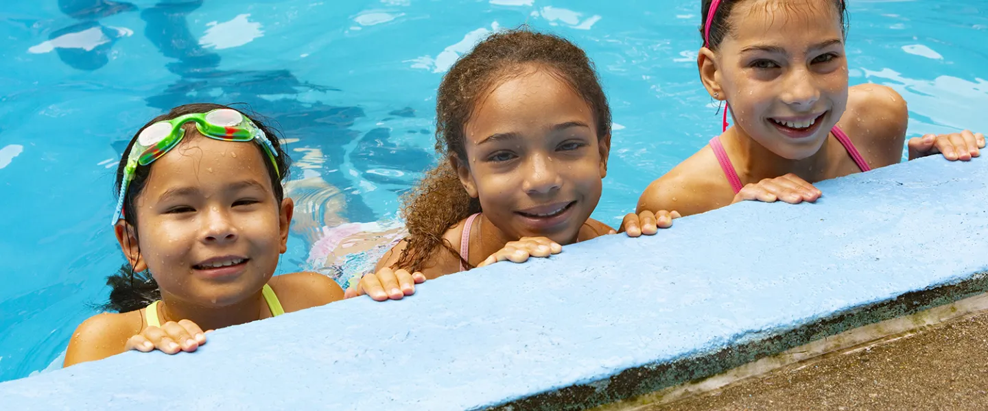 Three campers standing in the pool holding on to the wall.