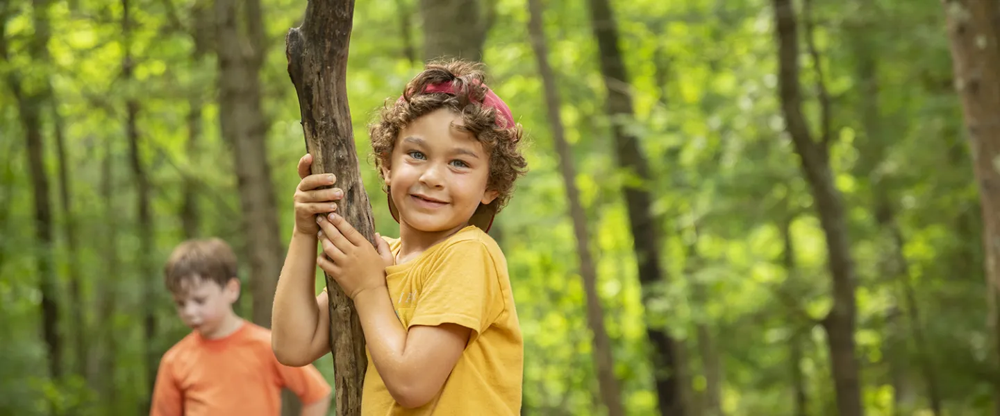 A camper holding onto a little tree and smiling right into the camera.