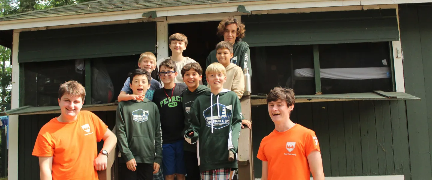 A group of campers and two consulars stand by their cabin.