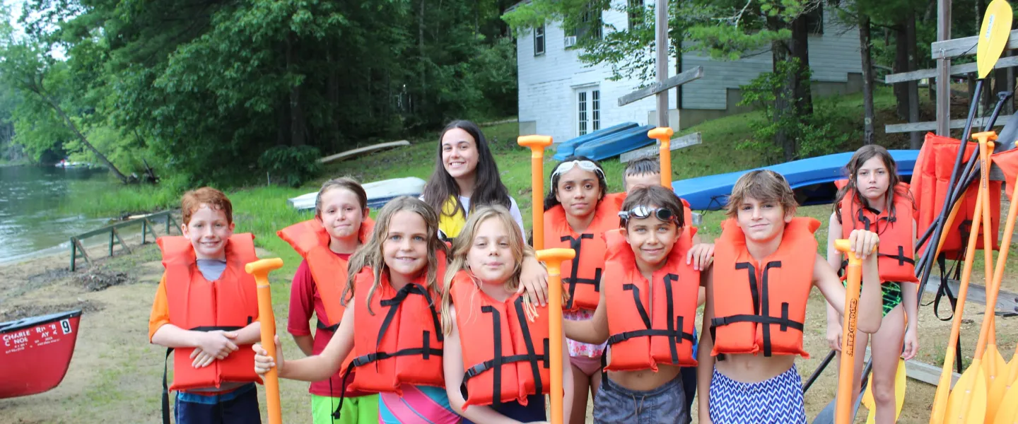 A large group of campers together getting ready to go kayaking in the lake.