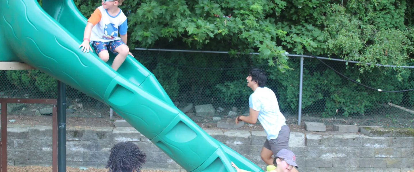 Camper riding down the slide in the playground.