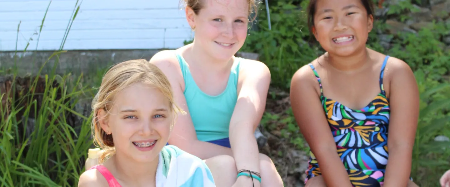 Three campers sitting getting ready to go for a swim in the lake.