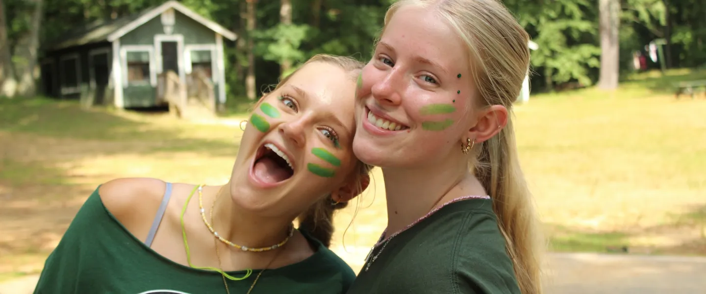 Two campers dressed both in green with some green eye paint pose together.