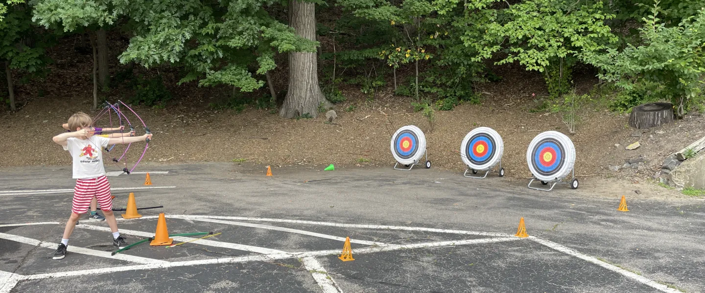 Three campers lined up shooting their bow n' arrow.