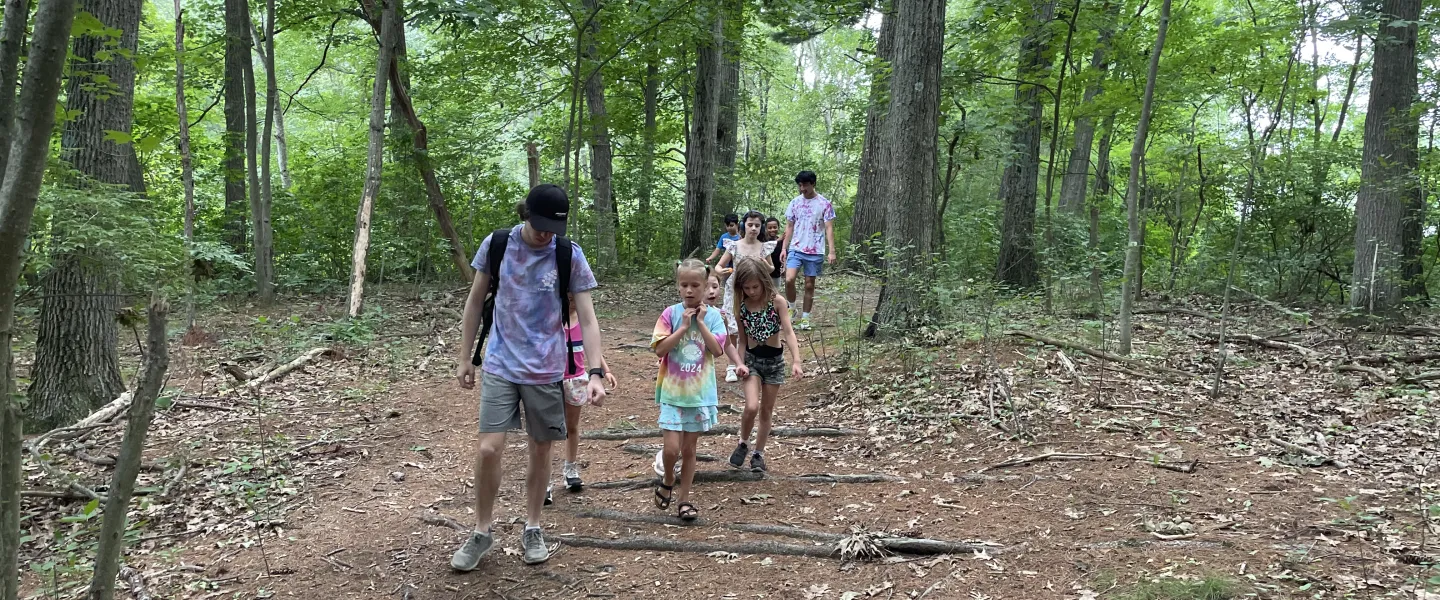 A group of campers and their consulars walking down the woods trail.