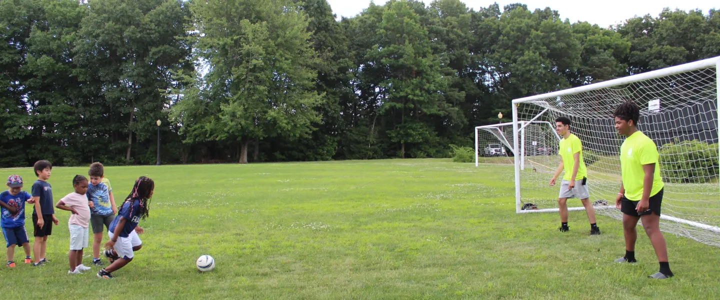 Camper lines up to kick a soccer ball as her consulars play goalie.