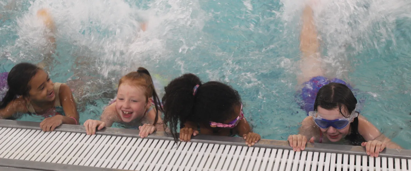 Campers holding on to edge of the pool kicking back water.