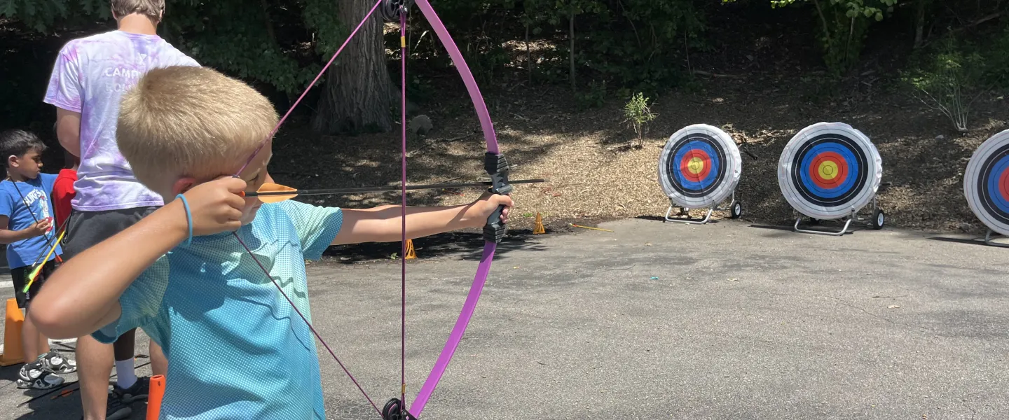 A camper pulls back his bow n' arrow getting ready to shoot.