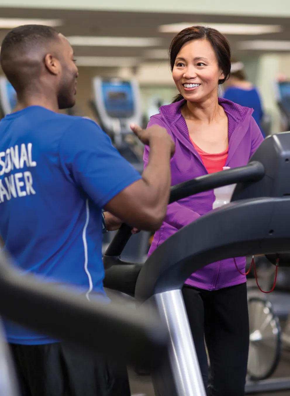 A personal trainer talks to a smiling woman who is on a treadmill
