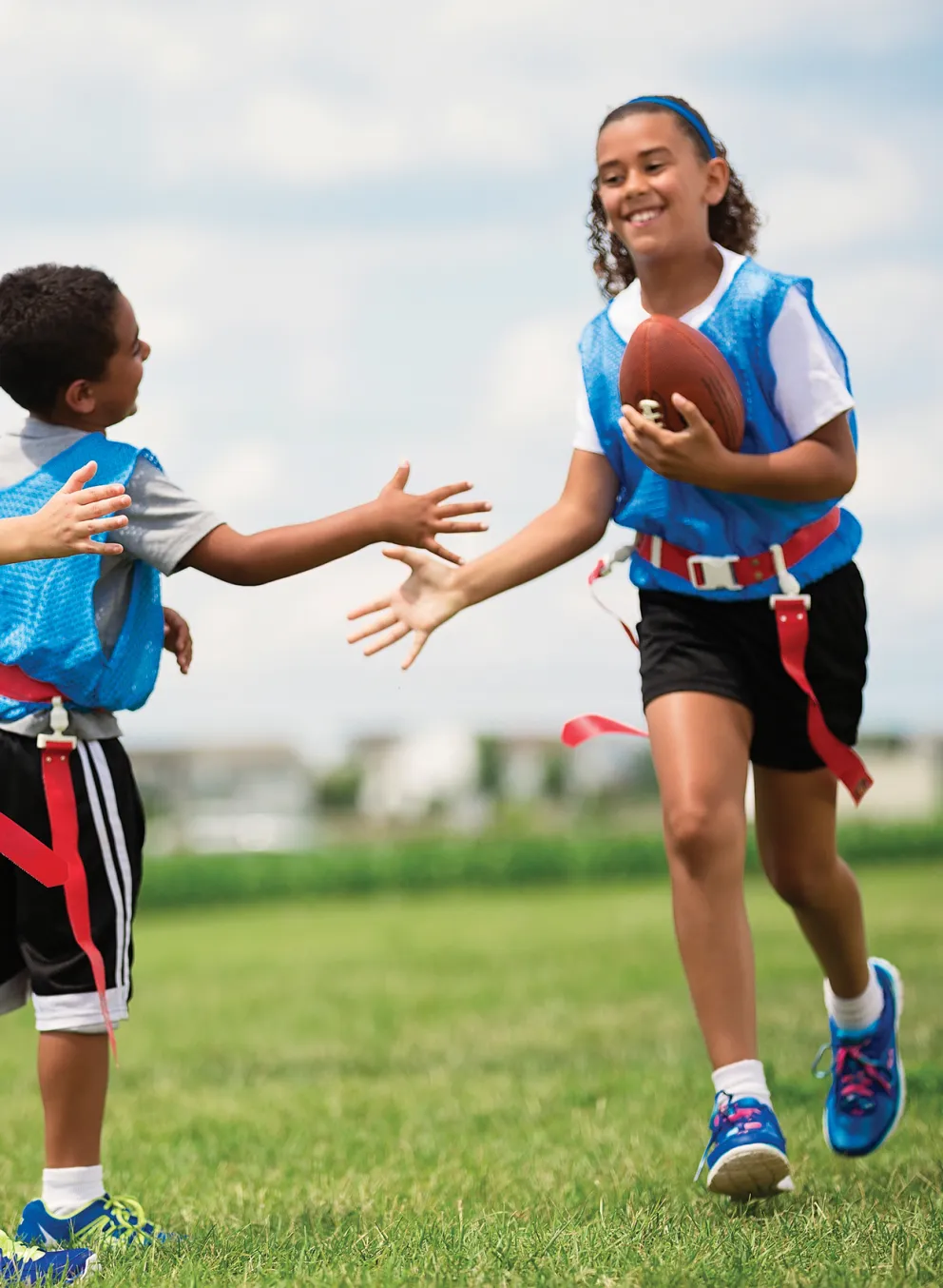 Girl carrying a football high fives two boys on her flag football team