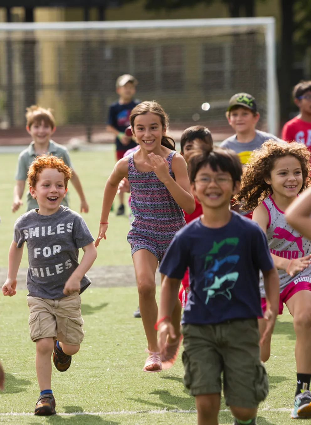 A group of school-age kids run across a field laughing and smiling