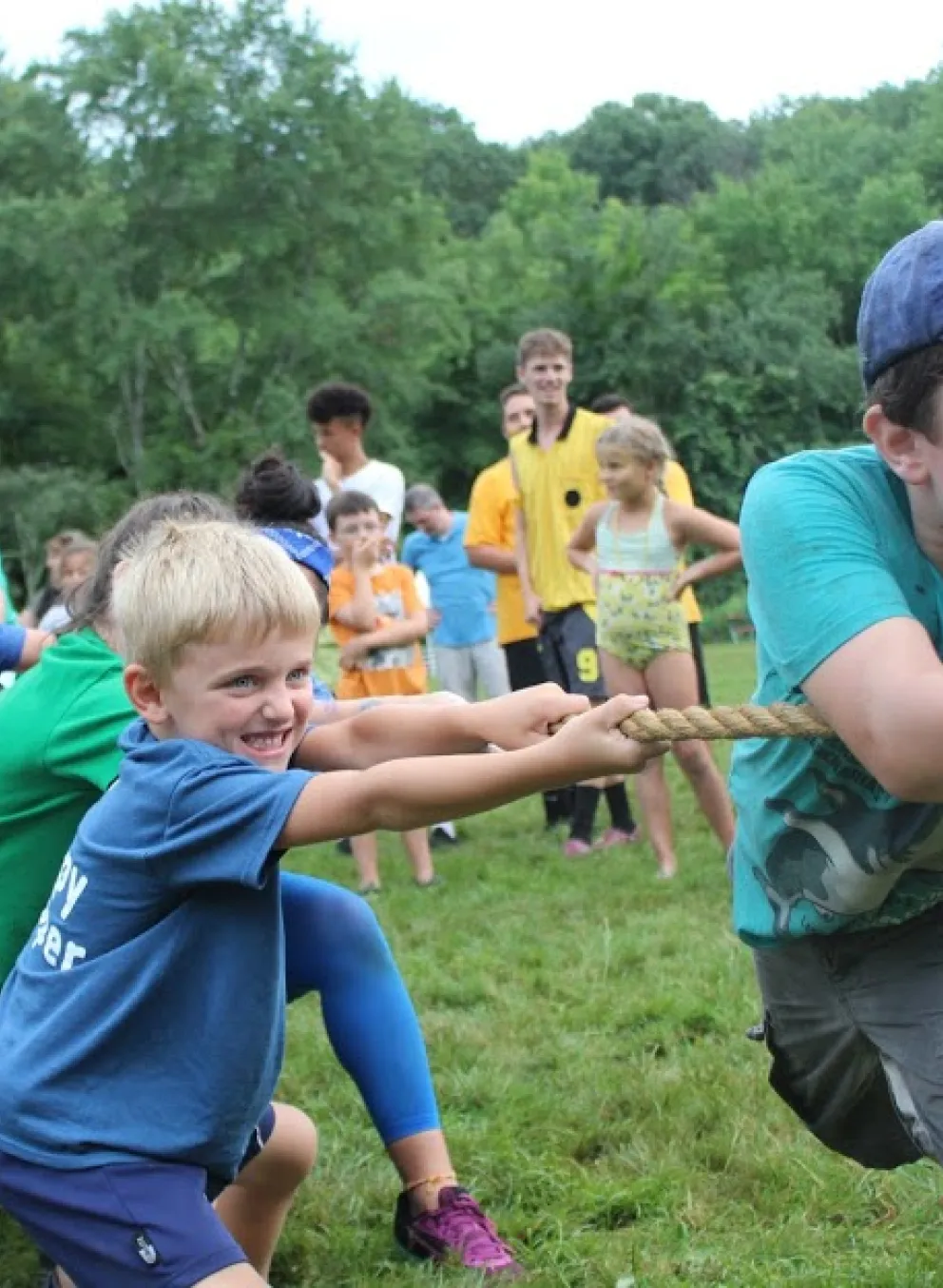 A group of children compete in tug of war, and one boy in the front grits his teeth while laughing.
