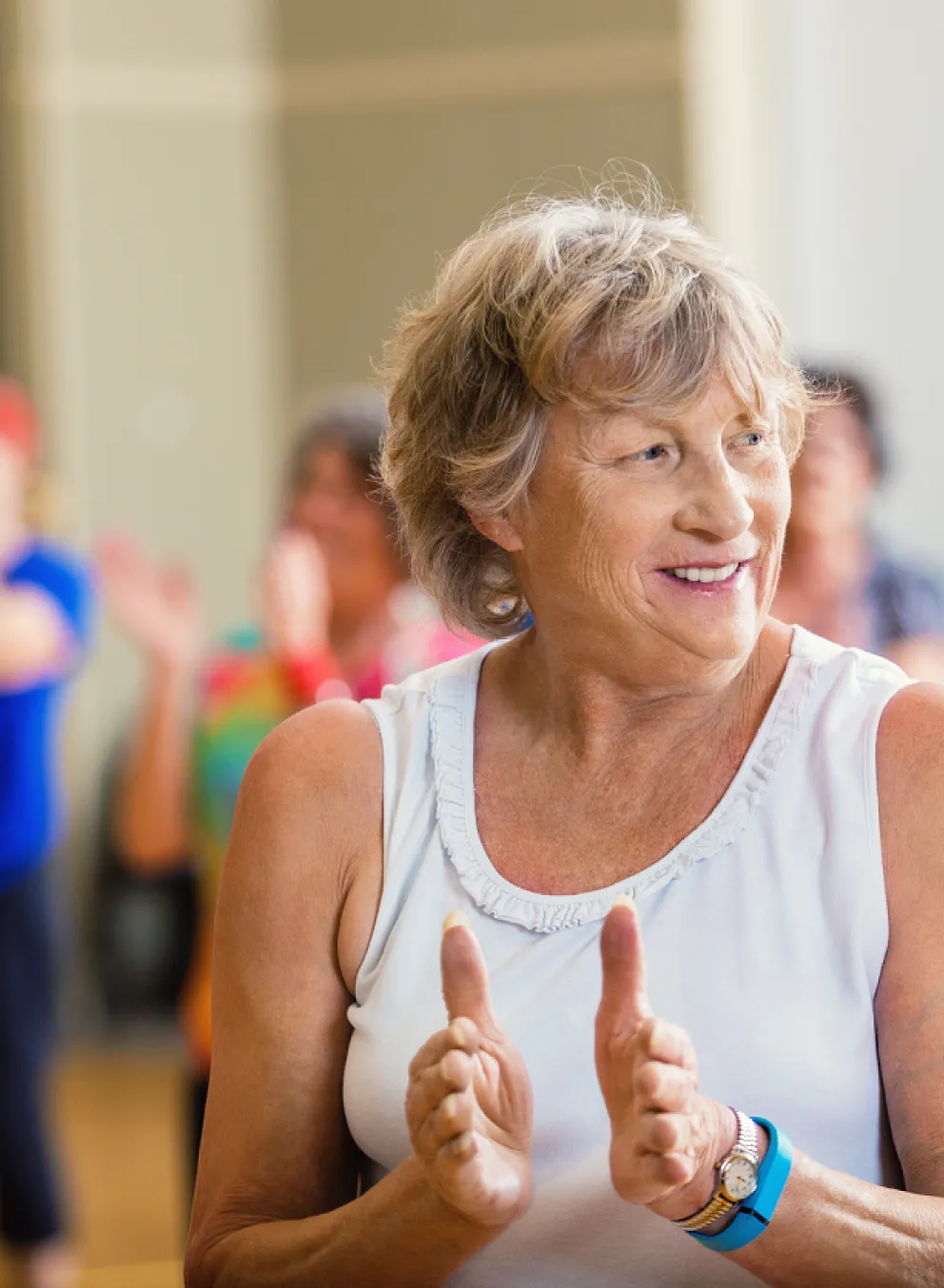 An older woman in focus claps along in a group exercise class