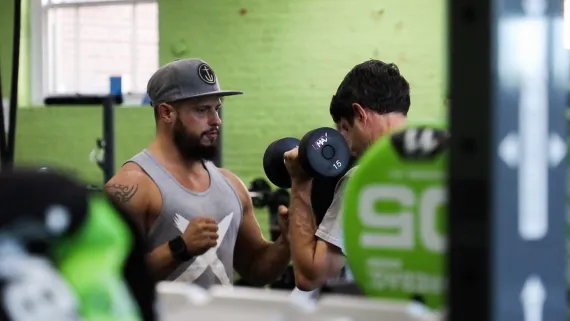 A personal trainer instructs a client who is holding a large dumbbell