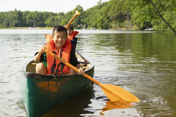 A camper smiles at the camera while paddling a canoe