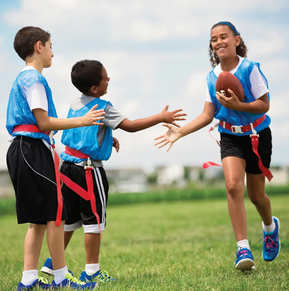 Girl carrying a football high fives two boys on her flag football team